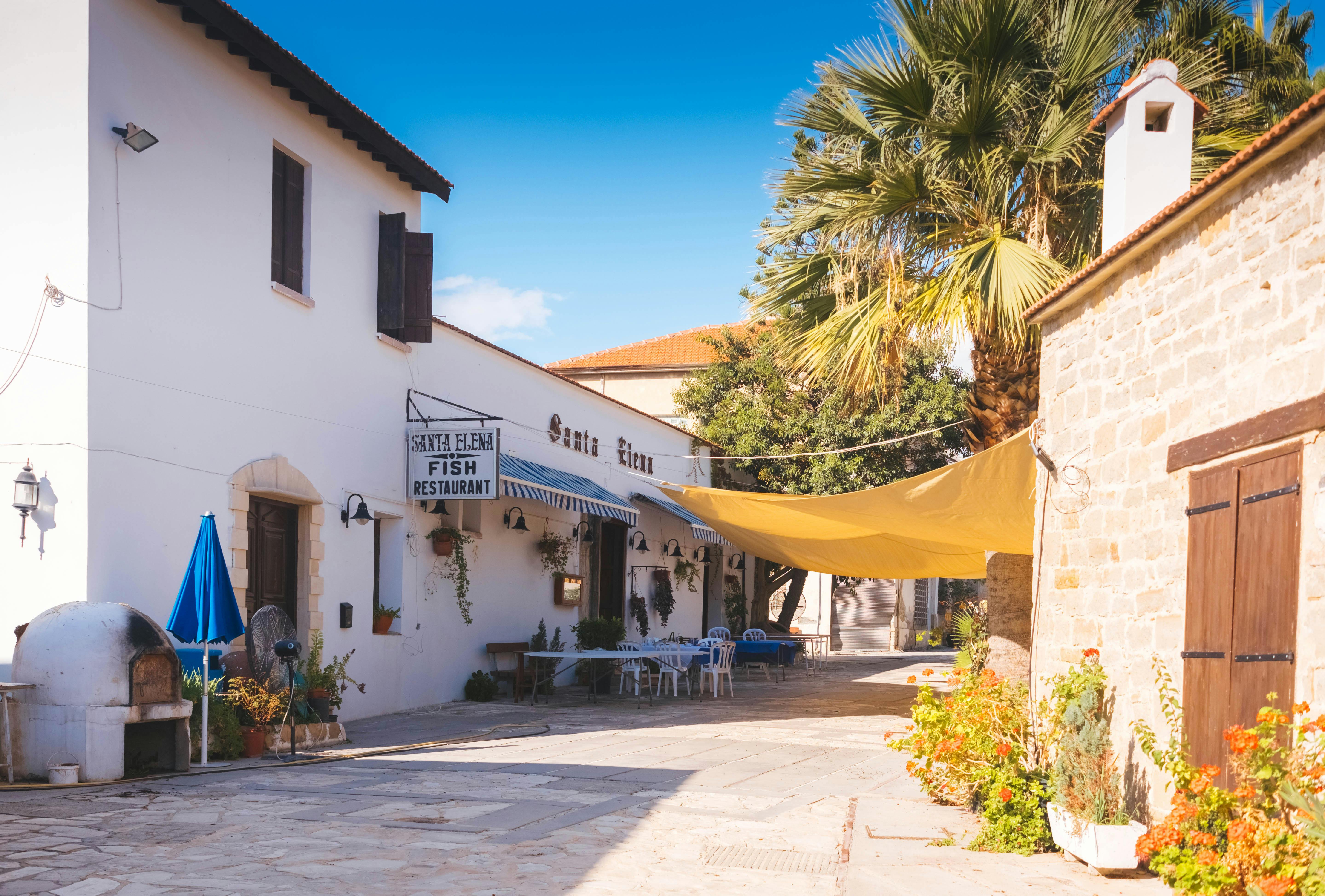 Free Exterior view of a quaint restaurant in Cyprus with outdoor seating, palm trees, and stone architecture. Stock Photo